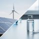 Glass vial and pipette on a lab workbench with a blurred view of solar panels and a distant wind turbine silhouette in the background.